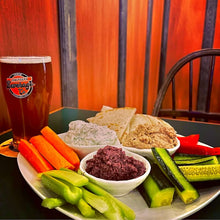 The Hat Trick trio of dips with veggies on a plate next to a beer. 